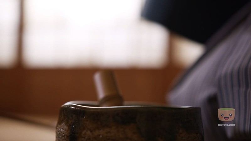 un homme en tenue cérémonial qui mélange le matcha dans un bol avec un fouet chasen.